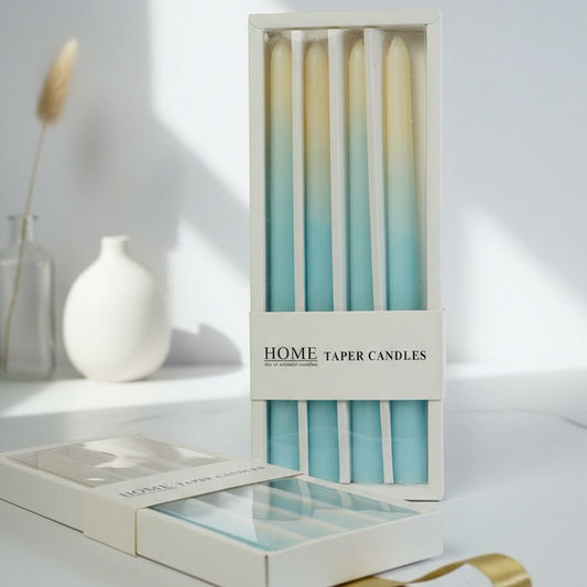 Set of home taper candles in a box on a white surface with a vase in the background